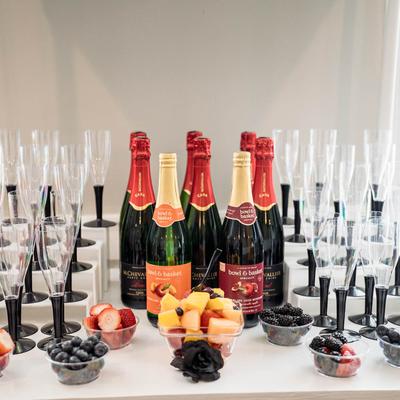 Bottles of sparkling wine and sparkling juices, fruit in plastic bowls, wine glasses.
