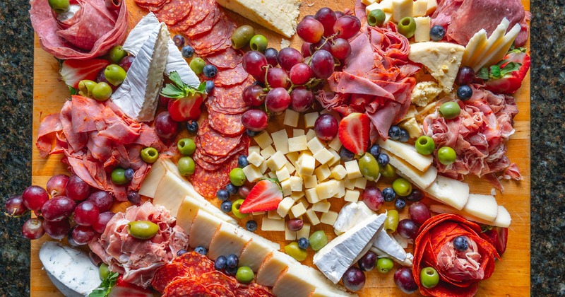 A top view of a colorful platter displaying a variety of charcuterie products, cheeses, and fruits