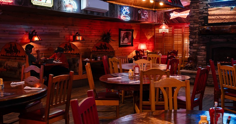 Rustic restaurant interior with wooden tables, chairs, neon beer signs, and a stone fireplace