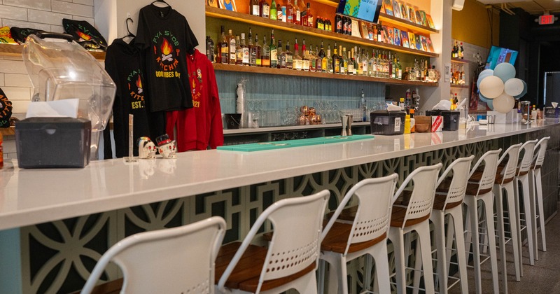 A modern bar with a white countertop, white bar stools, and shelves with liquor bottles