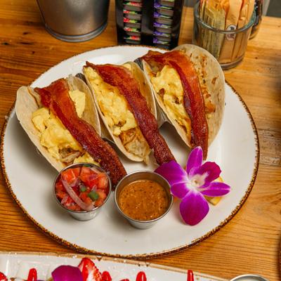 French Tacos topped with scrambled eggs and bacon, served with a dip and salsa.
