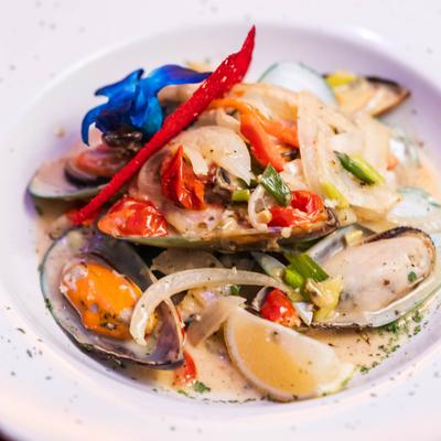 A bowl of mussels with peppers and herbs in a creamy sauce.