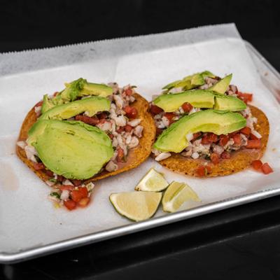 Tostada ceviche topped with avocado slices and served with lime wedges.