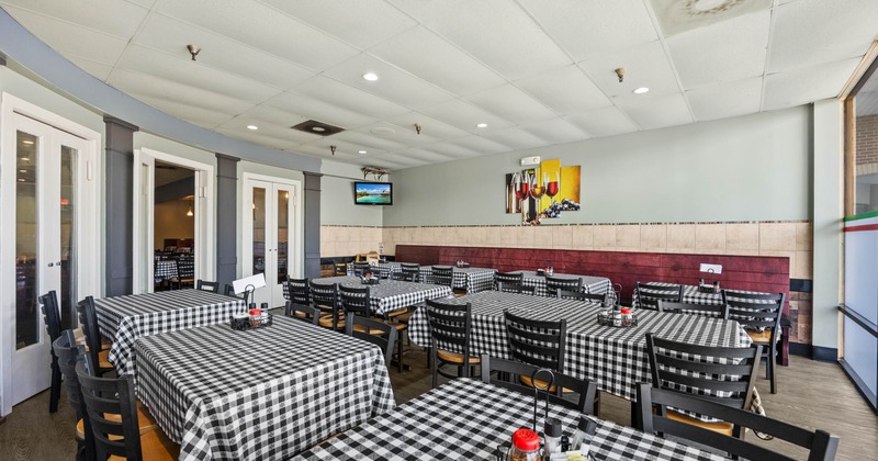 Inside, dining area with checkered tablecloths, black wooden chairs, and painting on the wall