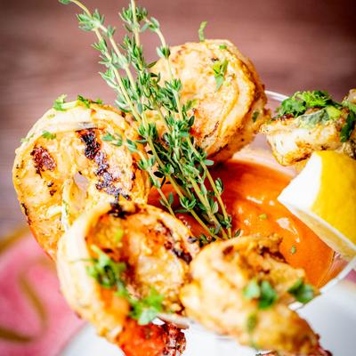 A close-up of a shrimp cocktail garnished with thyme and a lemon wedge.