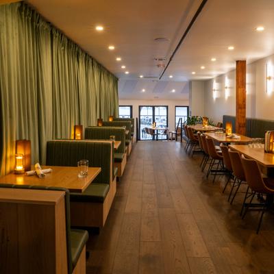 Dining room with green booths, wooden tables, and warm ambient lighting.