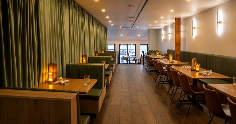 Interior of a modern restaurant with green booths, wooden tables, leather chairs