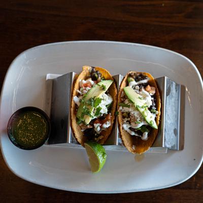 Two Carne Asada Tacos, served with lime wedge and salsa, top view.