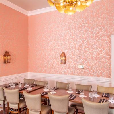 Interior, dining tables with place settings in a room with pink wallpaper and gold leaf chandelier