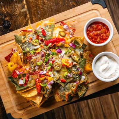 Colorful nachos with salsa and sour cream on a wooden board.