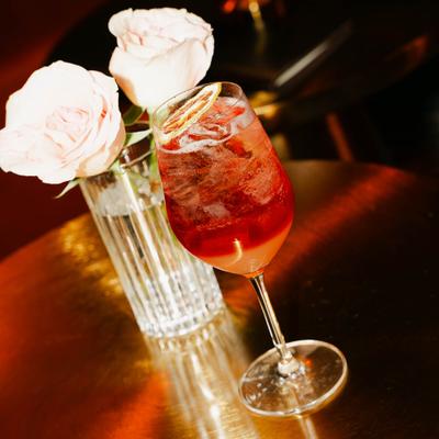 Aperol spritz beside a glass vase with white roses.