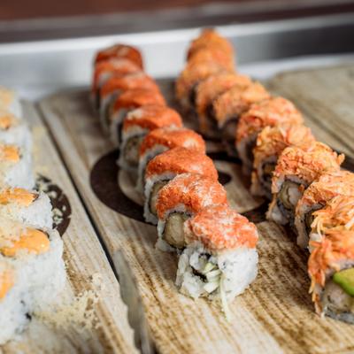 Three distinct rows of colorful sushi rolls sit displayed on wooden boards.