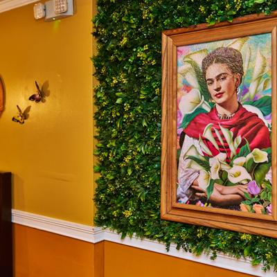 Frida Kahlo portrait on a green plant wall.