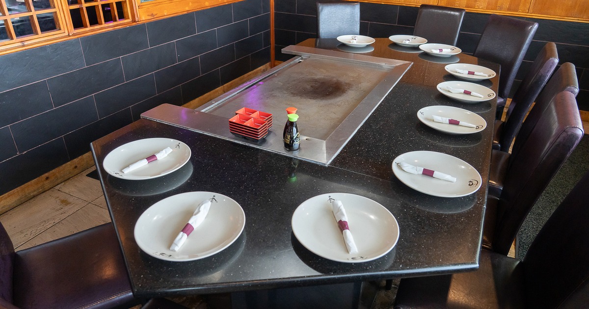 Large teppanyaki grill table set with white plates and napkins for ten guests