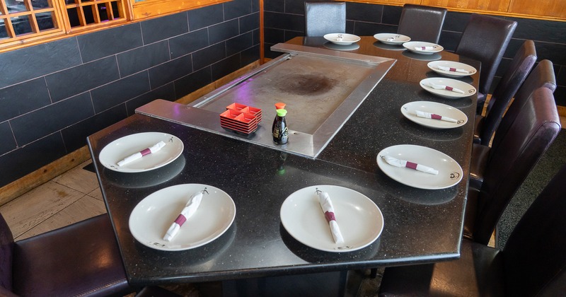 Large teppanyaki grill table set with white plates and napkins for ten guests