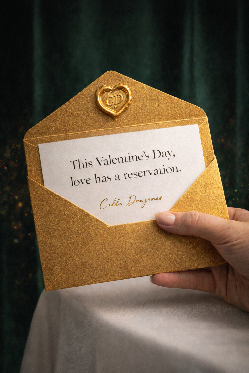 A white invitation envelope with a gold wax seal and a card inside that reads, This Valentine’s Day, love has a reservation.