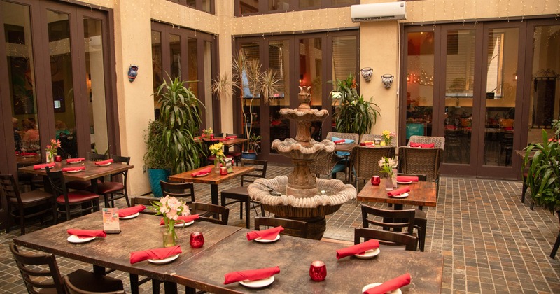 Outdoor dining area with wooden tables, red napkins, and a fountain
