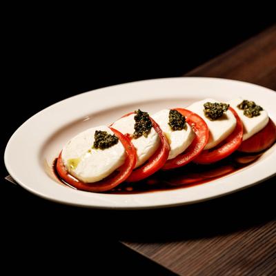 Caprese salad featuring sliced tomatoes, mozzarella, pesto and balsamic glaze.