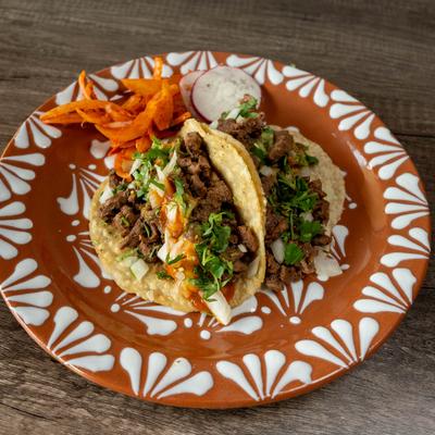 Two steak tacos topped with cilantro and chopped onions.