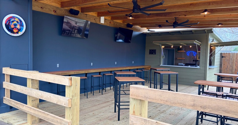 Covered patio with tall wooden tables facing a small outdoor bar window