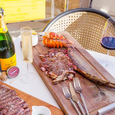 Tomahawk ribeye steak served alongside a lobster tail, champagne and red wine.