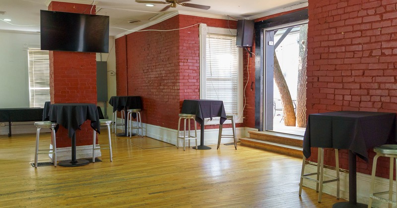 Interior, tables with black table cloths and stools, a TV screen