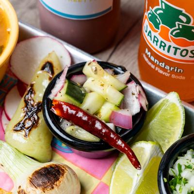 A bowl of soup, grilled onion, pickled cucumber salad with a chili, lime slices, cilantro.