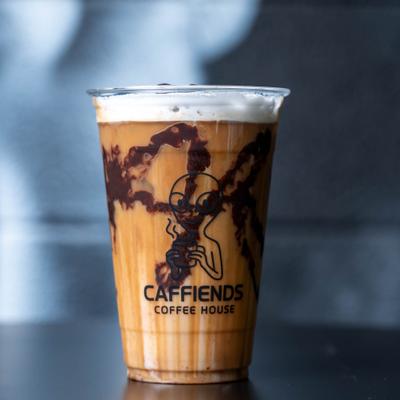 Iced coffee in a plastic cup with chocolate drizzle and foam.