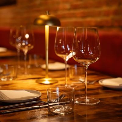 Warmly lit restaurant table with empty wine glasses, plates, and cutlery set on a wooden surface.