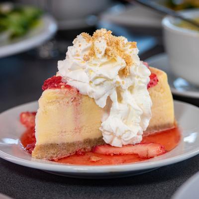Cheesecake slice topped with strawberry sauce, whipped cream, and crushed vanilla wafers.