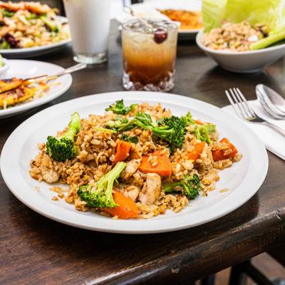 Stir-fried rice with chicken and vegetables served with a cocktail and side dishes.