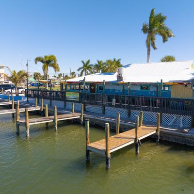 Waterfront restaurant with wooden docks and palm trees under clear blue sky.
