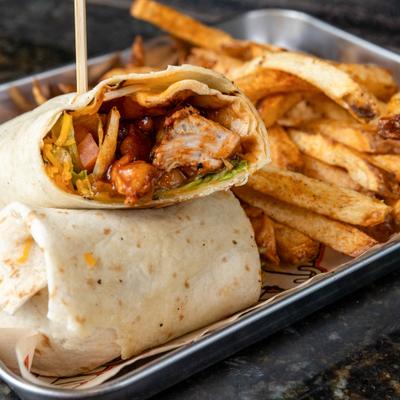 Barbecue chicken wrap cut in half, served with fries on a metal tray.
