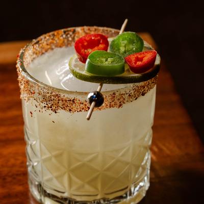 Cocktail in a rimmed glass garnished with slices of red and green chili and a lime wheel.