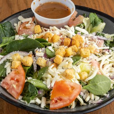 Spinach and feta salad with tomatoes, croutons, and sauce on the side.