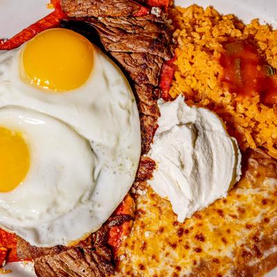 Tortilla chips smothered in red sauce, with steak, eggs, sour cream, rice, and beans.