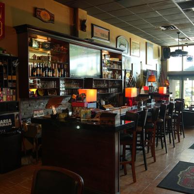 Bar area with wooden stools, liquor shelves, and warm-lit lamps.