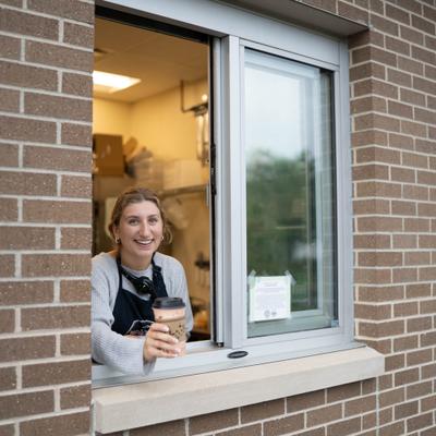 A smiling employee hands a cup through a drive-thru window in a brick building.