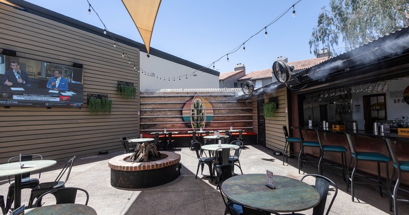 Outdoor bar patio with round tables and chairs, fire pit, wall-mounted TV