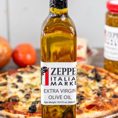 A bottle of Italian extra virgin olive oil, pizza and fresh vegetables in the background.