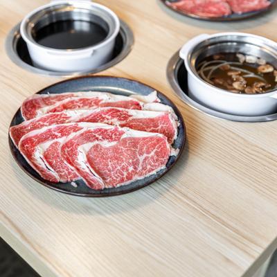 Side view of a table spread, meat plate with two pots of broth.