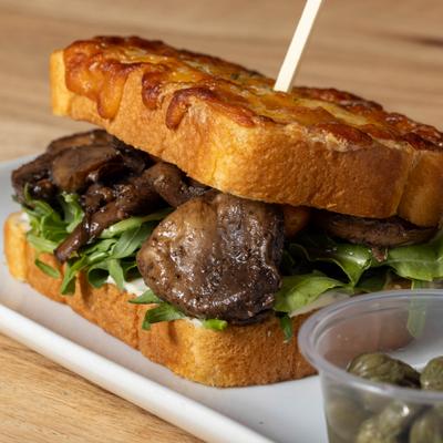 Mushroom And Tomato Sandwich served with a side of capers in a small container.