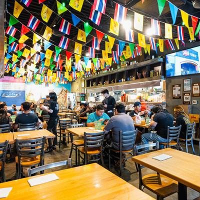 Busy Thai restaurant interior with colorful festival flags, wooden tables, and metal chairs.