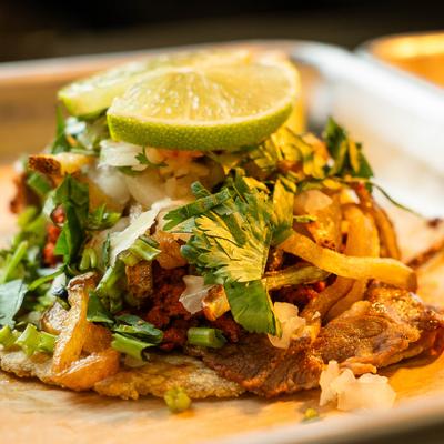 Taco featuring shredded meat topped with fresh onion, cilantro, and a lime wedge.