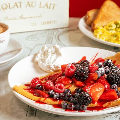 Plate of berry-loaded crepes served with a dollop of whipped cream.
