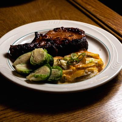 Charred grilled pork chop served alongside brussels sprouts and au gratin potatoes.