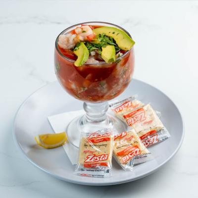 Shrimp cocktail with avocado slices and cilantro served with crackers.