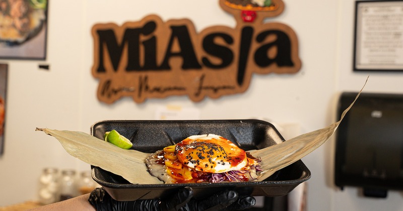 Hand holding a takeout container with Buldak Taco, restaurant sign is in the background