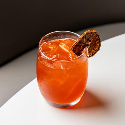 A red cocktail on the rocks with a dried orange wheel.