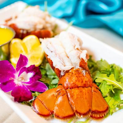 Cooked lobster tail with greens, lemon wedges, and a purple orchid garnish.